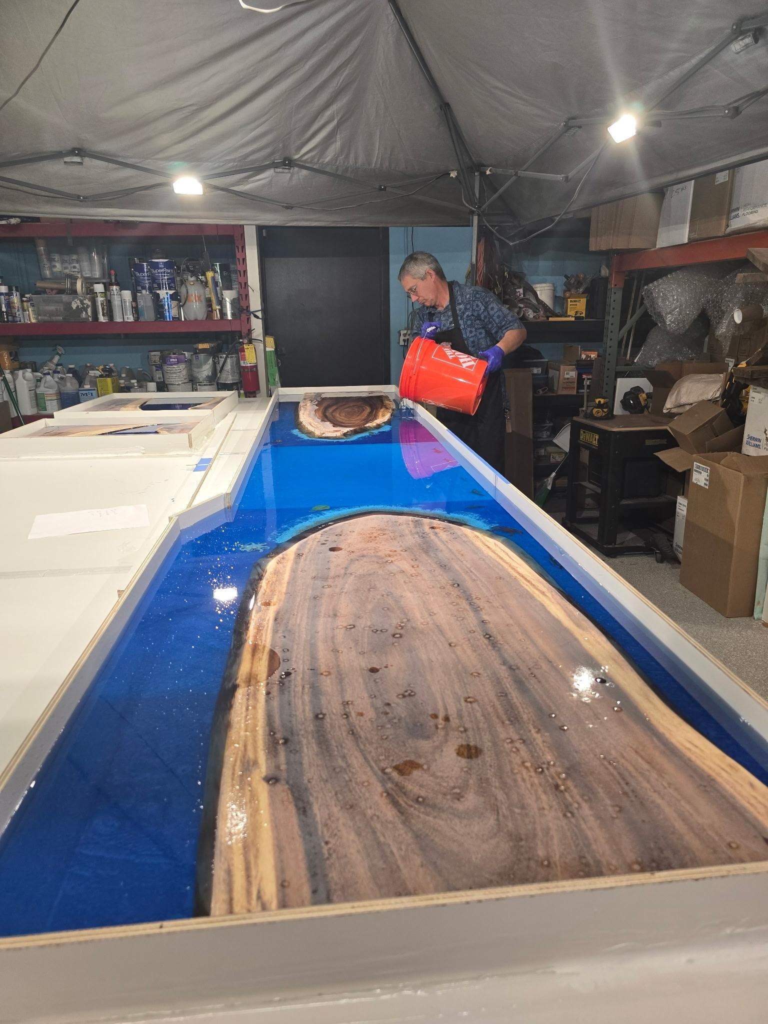 Pouring blue deep-pour epoxy around a live-edge monkeypod slab for a custom river table at Island Wide Resins in Kailua-Kona